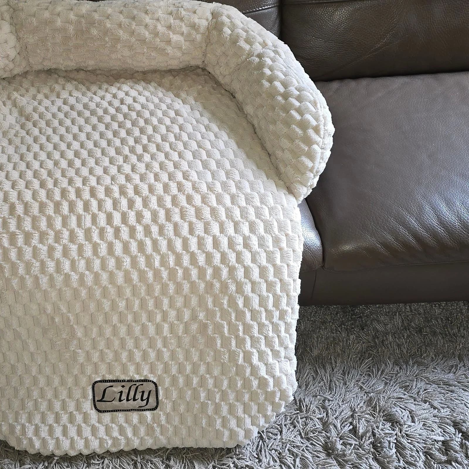Doudou fauteuil pilou gaufré écru posé sur un canapé cuir, plaque brodée — format panoramique